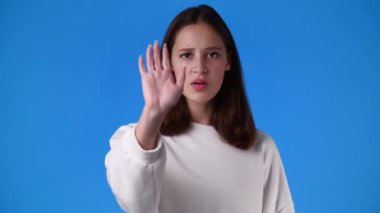 Negatif yüz ifadesi olan bir kızın 4k yavaş çekim videosu duruyor ve mavi arka planda yasaklanıyor. Duyguların kavramı.