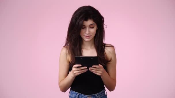 タブレットの上で何か素敵なものを読んでピンクの背景の上に笑顔1人の女の子の4Kビデオ 感情の概念 — ストック動画