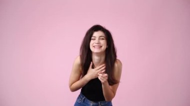 4K videoda bir kız gülüyor ve pembe arka planda parmağını öne doğru gösteriyor. Duyguların kavramı.