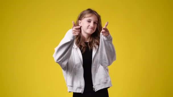 4K视频中 一个女孩竖起大拇指 在黄色背景下微笑 情绪的概念 — 图库视频影像