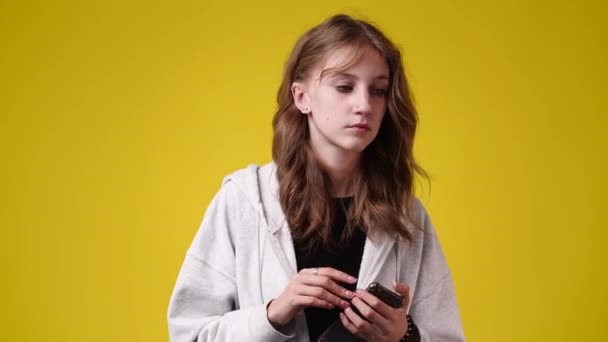 4K视频中的一个女孩一边拿着手机一边在黄色背景下用手弹奏 一边在想什么 情绪的概念 — 图库视频影像
