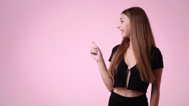 4Kビデオの可愛い女の子が左を向いてピンクの背景に親指を立てています 感情の概念 — ストック動画