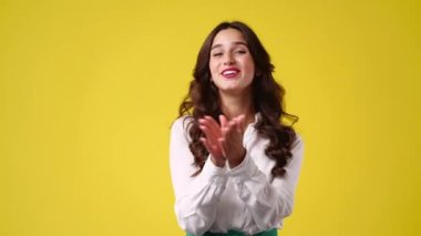 4k video of one girl claps his hands and smiling over yellow background. Concept of emotions.