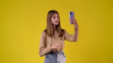 4k video of one girl who talking to someone on a video call over yellow background. Concept of emotions.
