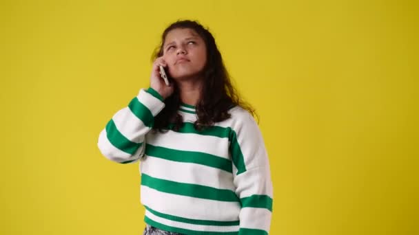 黄色の背景に否定的な顔の表情で電話で話している1人の感情的な女の子の4Kビデオ 感情の概念 — ストック動画