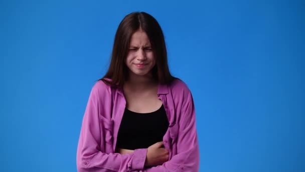4K视频 一个女孩痛苦不堪 双手放在蓝色背景的腹部 情绪的概念 — 图库视频影像