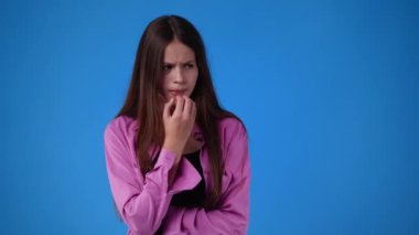 Genç bir kızın endişelendiği 4K videosu mavi arka planda elini yüzüne koyuyor. Duyguların kavramı.