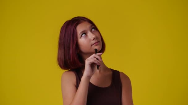 黄色い背景の上にペンを手に持っている少女の4Kビデオ 感情の概念 — ストック動画