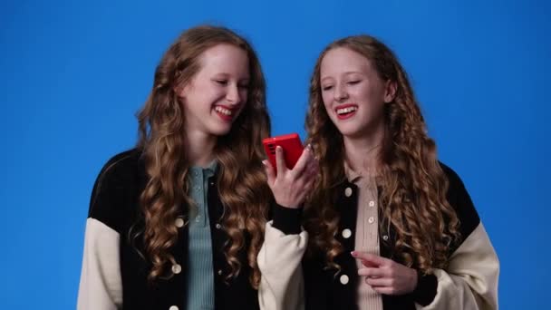 Video Von Zwillingsmädchen Die Auf Blauem Hintergrund Telefonisch Musik Hören — Stockvideo