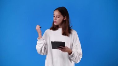 4k video of one girl which thinks and notes something with a pen on tablet over blue background. Concept of emotions.