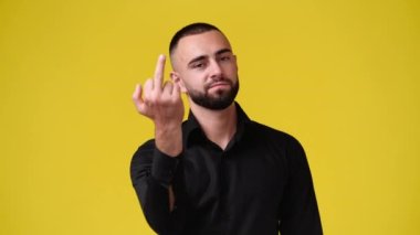 Yüzünde negatif ifade olan bir adamın 4K videosu orta parmağını sarı arka planda gösteriyor. Duyguların kavramı.