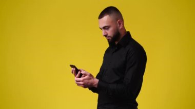 Sarı arka planda telefonuyla video izleyen bir adamın 4K videosu. Duyguların kavramı.