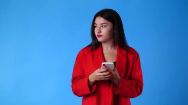 Bir kadının 4k 'lık videosu sol tarafı işaret ediyor. Telefonu elinde tutuyor ve mavi arkaplanı işaret ediyor. Duyguların kavramı.