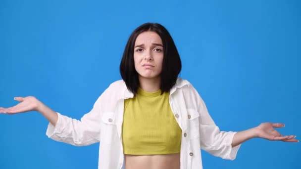 一个年轻女孩在蓝色背景下怀疑并挥动双手的4K视频 情绪的概念 — 图库视频影像