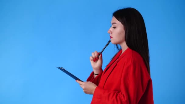 青い背景の上にタブレットでペンで何かを考え メモする1人の女性の4Kビデオ 感情の概念 — ストック動画