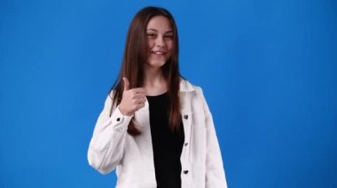 4k video of one girl pointing at right and showing thumb up over blue background. Concept of emotions.