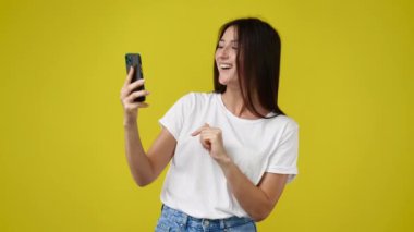 Sarı arka planda telefonu kullanıp el sallayan hoş bir kızın 4K videosu. Duyguların kavramı.