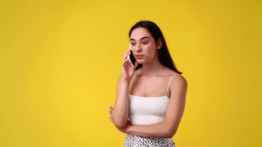 Sarı arka planda telefonla konuşan bir kızın 4K videosu. Duyguların kavramı.