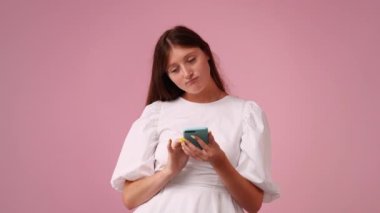 Pembe arka planda telefonu kullanan güzel bir kızın 4K videosu. Duyguların kavramı.