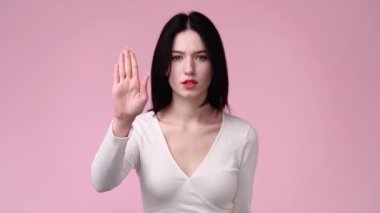 Pembe arka planda çapraz elleri olan bir kızın 4K videosu. Olumsuz duygu kavramı.