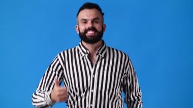 Mavi arka planda baş parmağını gösteren bir adamın 4K videosu. Olumlu duygu kavramı.