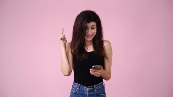 ピンクの背景の上に彼女の携帯電話を使用して1人の女の子の4Kビデオ 感情の概念 — ストック動画