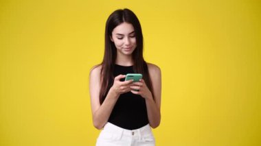 Sarı arka planda telefonunu kullanan bir kızın 4K videosu. Duyguların kavramı.