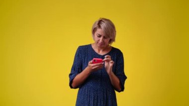 Sarı arka planda telefonunu kullanan bir kadının 4K videosu. Duyguların kavramı.