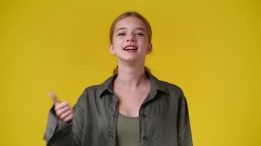 4k video of one girl showing thumbs up over yellow background. Concept of emotions.