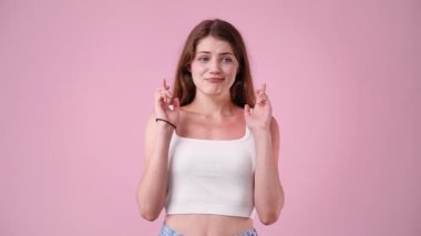 Bir kadının 4K videosu parmaklarını çapraz yapar ve pembe arka planda bir şeye inanır. Duyguların kavramı.
