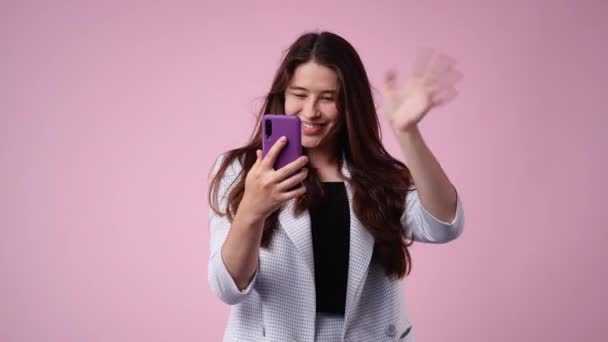 ピンクの背景でビデオ通話で誰かと話している1人の女の子の4Kビデオ 感情の概念 — ストック動画