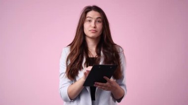 Pembe arka planda elinde tabletle OK işareti gösteren bir kızın 4K yavaş çekim videosu. Duyguların kavramı.