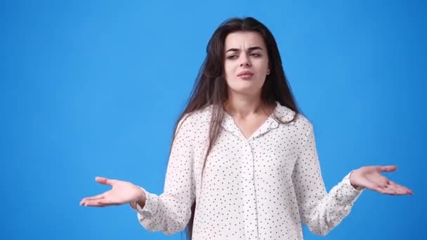 一个年轻女孩在蓝色背景下怀疑并挥动双手的4K视频 情绪的概念 — 图库视频影像