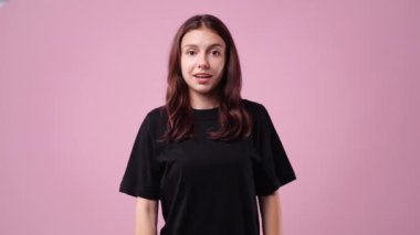 Pembe arka planda duygusal olarak sevinen bir kızın 4K yavaş çekim videosu. Duyguların kavramı.