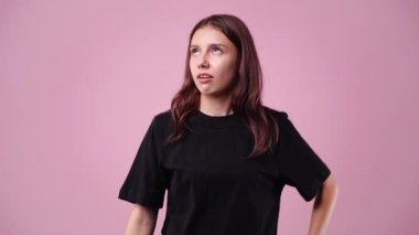 Pembe arka planda poz veren neşeli bir kızın 4K yavaş çekim videosu. Duyguların kavramı.