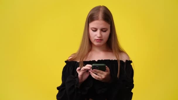 黄色い背景の上の電話からのメッセージに驚いた1人の少女の4K動画 感情の概念 — ストック動画