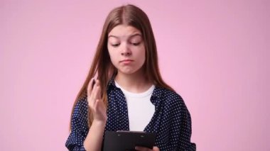 4k video of one girl which thinks and notes something with a pen on tablet over pink background. Concept of emotions.