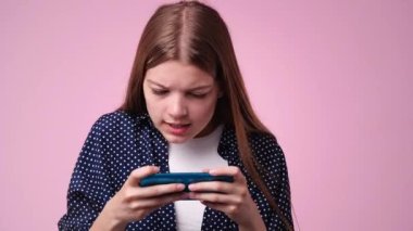 4k video of one girl is playing on the phone over pink background. Concept of emotions.