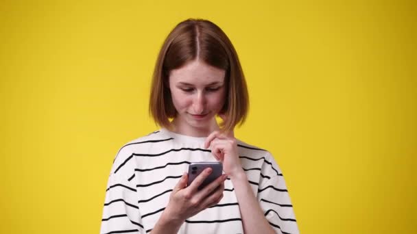 1人の女の子が電話でテキストを入力し 黄色の背景に笑みを浮かべての4Kビデオ 感情の概念 — ストック動画