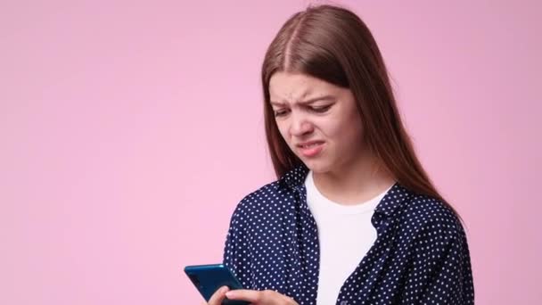 ピンクの背景に否定的な表情のテキストを入力した1人の女の子の4Kビデオ 感情の概念 — ストック動画