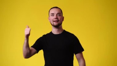 Sarı arka planda baş parmağını gösteren bir adamın 4K videosu. Duyguların kavramı.