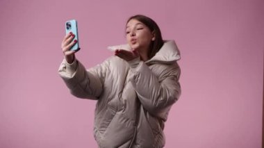 Pembe arka planda telefonunu kullanan bir kızın 4K videosu. Duyguların kavramı.