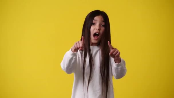 4K视频 一个女孩指着右边 在黄色背景上伸出大拇指 情绪的概念 — 图库视频影像