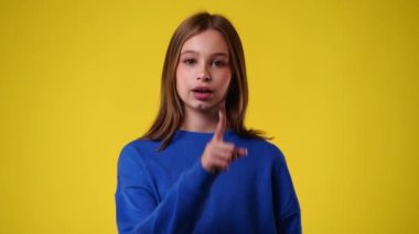 Sarı arka planda sessizlik işareti gösteren bir kızın 4K videosu. Duyguların kavramı.