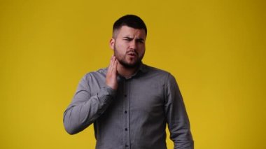 Sarı arka planda çenesine dokunan bir adamın 4K videosu. Duyguların kavramı.