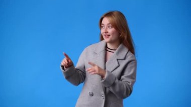 Bir kızın mavi arka planda kaldırma ve işaret ettiği 4K videosu. Duyguların kavramı.