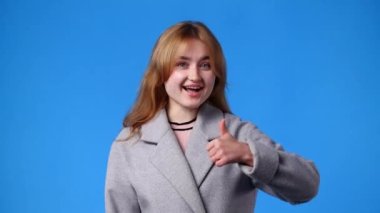 4K video 'da bir kız kamerayı işaret ediyor ve mavi arka planda başparmak gösteriyor. Duyguların kavramı.