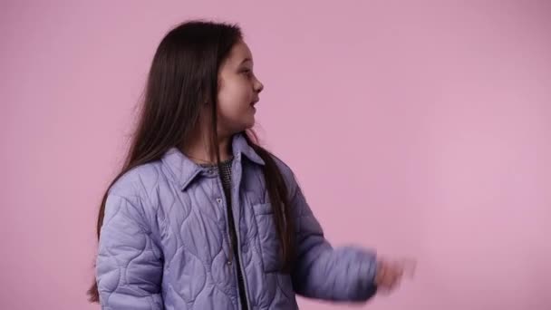 4K视频 一个女孩指着右边 用大拇指在粉色背景上显示 情绪的概念 — 图库视频影像