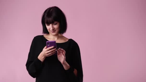 ピンクの背景に携帯電話を使ってある女性の4K動画 感情の概念 ピンクの背景に彼女の携帯電話を使用して1人の女性の4Kビデオ — ストック動画