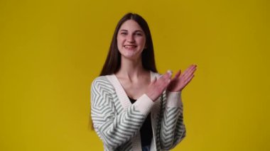 4k slow motion video of one girl claps his hands and smiling over yellow background. Concept of emotions.